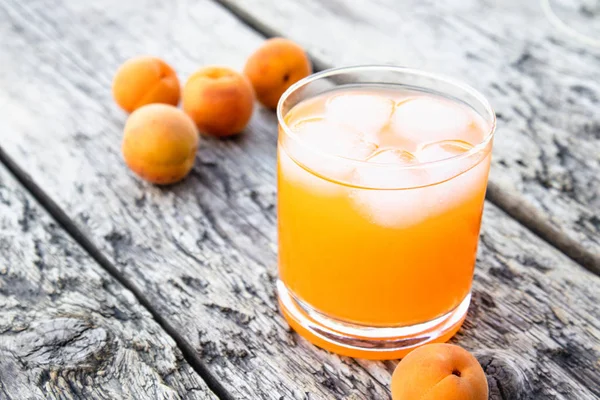 Fresh apricot juice with apricots and ice cubes in a glass against the background of old boards. Summer soft drinks.