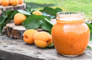 Cam bir kavanozda kayısı reçeli ve ahşap bir masada olgun kayısı.