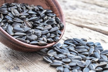 Tahta bir arka plan üzerinde bir kase ayçiçeği tohumu yığını. Masaya serpişne ayçiçeği tohumu.
