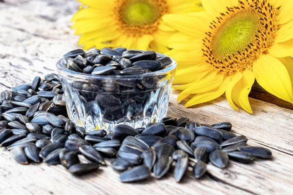 Yellow sunflowers and sunflower seeds in a glass container on a wooden background.