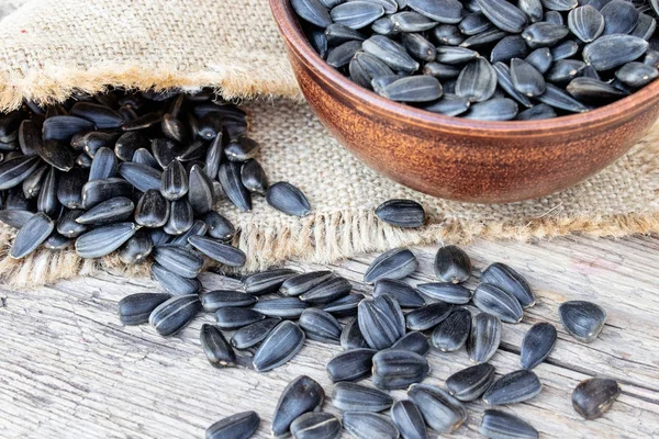 A pile of sunflower seeds in a bowl on a wooden background. Sunflower seeds scattered on the table.