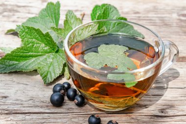 Siyah frenk üzümü yaprakları ile bir fincan çay. Ahşap bir masada kuş üzümü ile çay.