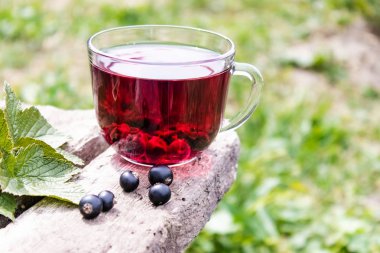 Açık havada ahşap bir masada siyah frenk üzümü çilek ile meyve çay Cam fincan. Close.