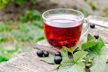 Yeşil yaprakları ve frenk üzümü meyveleri yakın ahşap bir masada frenk üzümü çilek ile meyve çay Cam fincan.
