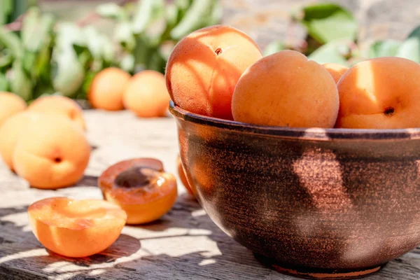 Вкусные спелые абрикосы в миске рядом с зелеными листьями на деревянном столе . — стоковое фото