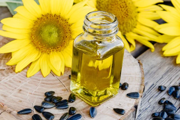 Aceite de girasol orgánico en un frasco de vidrio con semillas y flores frescas sobre un fondo de madera. Alimentos y grasas saludables . — Foto de Stock