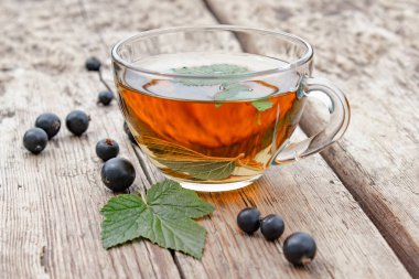 Yeşil frenk üzümü yaprakları ve meyveleri yakın ahşap bir masa üzerinde bir cam şeffaf fincan frenk üzümü yaprağı bitkisel çay.