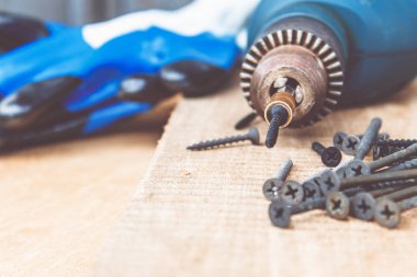 Bir çelik vida ahşap bir tahta arka plan üzerinde dağınık vidalar yakın bir elektrikli matkap yerleştirilir. Alet ve onarım çalışmaları kavramı. Çelik vidalar.