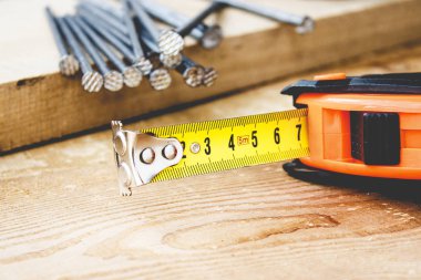 Tahta arka planda büyük çiviler ve sarı rulet cetveli. İnşaat işleri için araçlar.