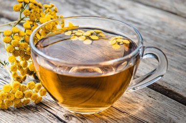 Ahşap bir masa üzerinde sarı tansy çiçekleri yakınında tansy şifalı otlar ile çay Fincan. Şifa otlar.