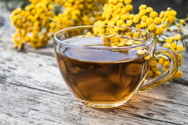 Ahşap bir masa üzerinde tansy ve tansy çiçekleri ile çay fincan. Şifa otlar.