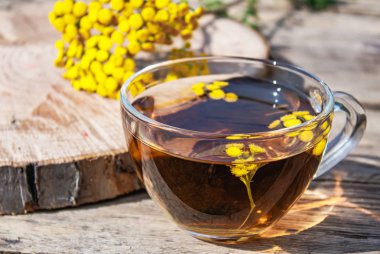Bir cam bardak ve ahşap bir masa üzerinde sarı tansy çiçekler tabak infüzyon. Tansy Bitkisel çay. Şifa otlar.
