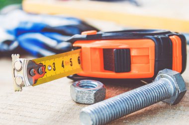 Çelik cıvata lar ve somunlar, bant ölçüsü cetvelinin yanındaki tahta tahtalarda yatıyor.