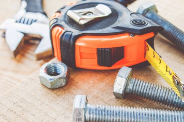 Çelik cıvata somunları ve yıkıtaları ayarlanabilir bir anahtar ve bant ölçüsü yakınında ahşap tahtalar üzerinde yalan.