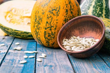 Mavi eski tahtalarda olgun bir kabak yakın bir kase içinde kabak tohumları.