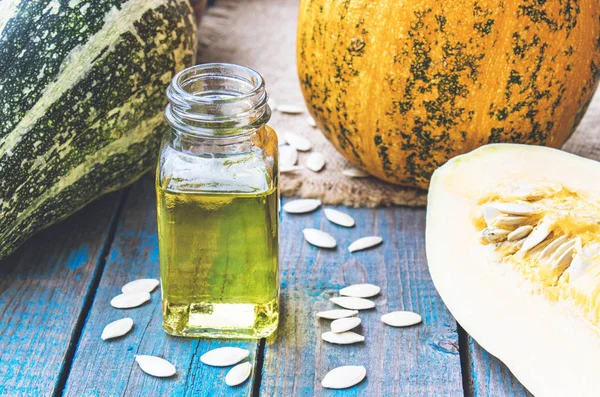 Mavi eski tahtalarda bir kabak yakın bir şişede kabak çekirdeği uçucu yağ.