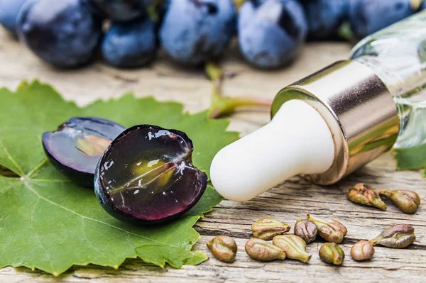 Grape seed oil in a glass bottle near blue grapes and green leaves on old wooden boards. Spa, eco products concept.