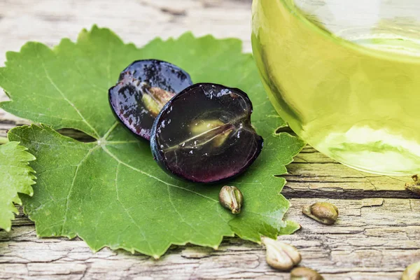Szőlőmag olaj egy üvegpalack közelében kék szőlő és a zöld levelek a régi fa deszkák. Spa, öko termékek koncepció. — Stock Fotó
