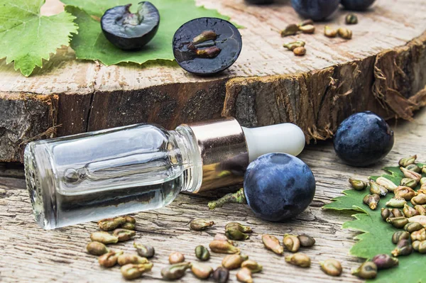 Mavi üzüm ve yeşil yapraklarıgrones yakın eski ahşap tahtalarda üzüm çekirdeği esansiyel yağı ile Şişe. Spa, eko ürünler konsepti.