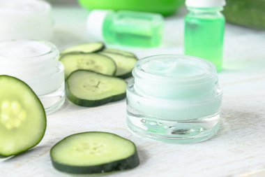 Beyaz ahşap arka planda taze salatalık dilimleri yanında salatalık özü ile bir cam kavanoz yüz kremi.