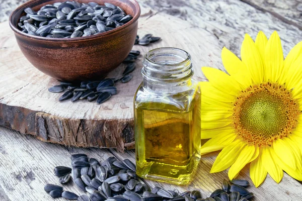 Girasoles y semillas sobre un fondo de madera cerca del aceite de girasol en un frasco de vidrio. Alimentos y grasas saludables . — Foto de Stock