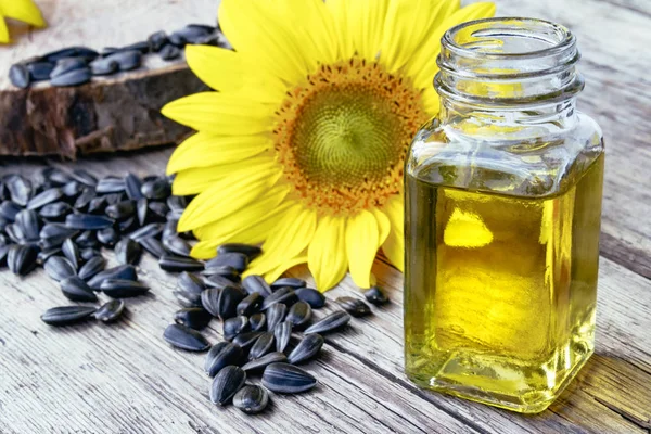 Sunflower oil in a glass jar with seeds and fresh flowers on a wooden background. Healthy foods and fats. — Stock Photo, Image