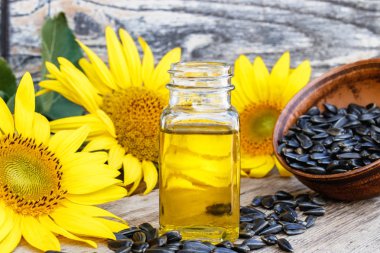 Taze ayçiçeği çiçekleri yakınında ahşap bir arka plan üzerinde bir kase ayçiçek yağı ve ayçiçeği tohumu. Organik ve eko gıda.