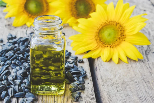 Slunečnicový olej ve skleněné nádobě se semeny a čerstvými květy na dřevěném podkladu. Zdravé potraviny a tuky. — Stock fotografie