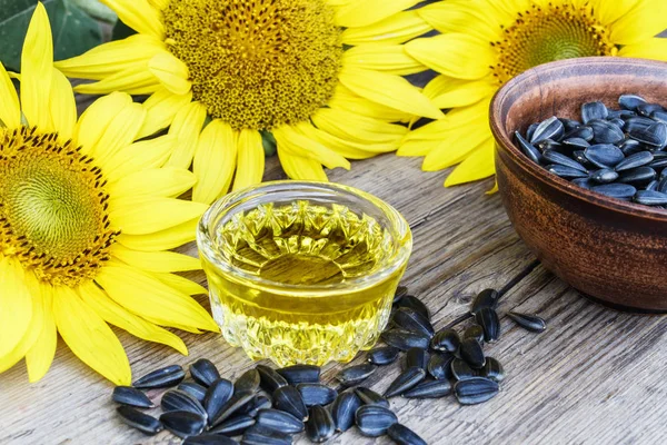 Aceite de girasol y semillas de girasol en un tazón sobre un fondo de madera cerca de flores frescas de girasol. Alimentos ecológicos y ecológicos . — Foto de Stock