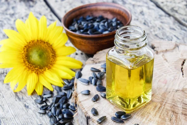 Aceite de girasol y semillas de girasol en un tazón sobre un fondo de madera cerca de flores frescas de girasol. Alimentos ecológicos y ecológicos . — Foto de Stock