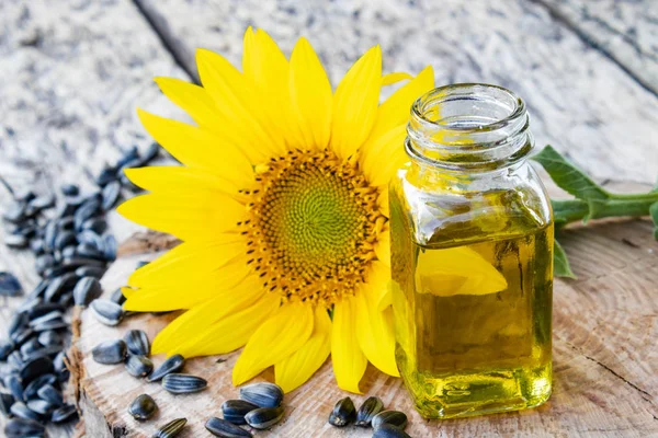 Tournesols et graines sur fond de bois près de l'huile de tournesol dans un bocal en verre. Aliments et graisses sains . — Photo