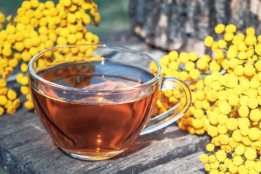 Ahşap bir masa üzerinde cam bir bardak tansy infüzyon. Tansy Bitkisel çay. Şifa otlar.