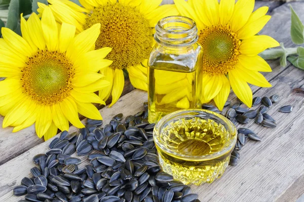 Sunflower oil with seeds on a wooden background near fresh sunflower flowers. Organic and eco food. — Stock Photo, Image