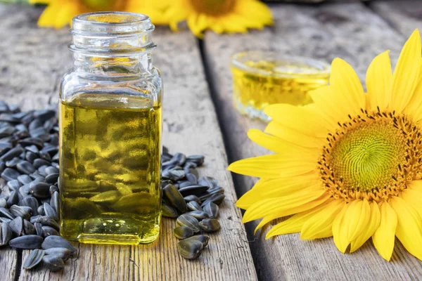 Huile de tournesol dans un pot en verre avec des graines et des fleurs fraîches sur un fond en bois. Aliments et graisses sains . — Photo