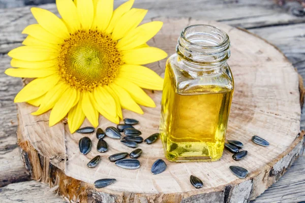 Органическое подсолнечное масло в стеклянной банке с семенами и свежими цветами на деревянном фоне. Здоровые продукты питания и жиры . — стоковое фото