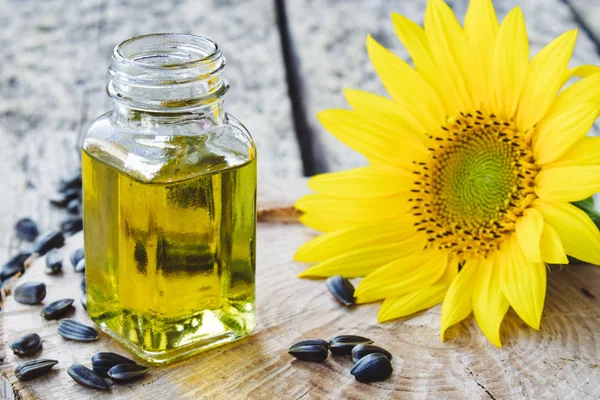 Óleo de girassol orgânico em um frasco de vidro com sementes e flores frescas em um fundo de madeira. Alimentos e gorduras saudáveis . — Fotografia de Stock