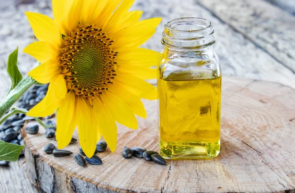 Slunečnice a semena na dřevěném pozadí u slunečnicového oleje ve skleněné sklenici. Zdravé potraviny a tuky. — Stock fotografie
