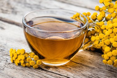 Ahşap bir masa üzerinde sarı tansy çiçekleri yakınında tansy şifalı otlar ile çay Fincan. Şifa otlar.