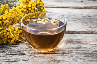 Ahşap bir masa üzerinde sarı tansy çiçekleri yakınında tansy şifalı otlar ile çay Fincan. Şifa otlar.