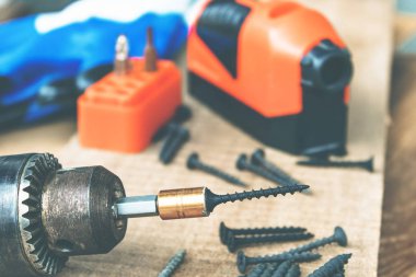 Bir çelik vida ahşap bir tahta arka plan üzerinde bir elektrikli matkap yerleştirilir. Alet ve onarım çalışmaları kavramı. Çelik vidalar.