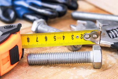 Çelik cıvata somunları ve yıkıtaları ayarlanabilir bir anahtar ve bant ölçüsü yakınında ahşap tahtalar üzerinde yalan.