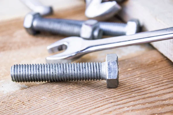 Steel bolts and nuts lie on wooden boards next to an adjustable wrench.
