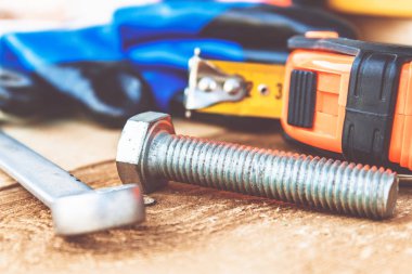 Çelik cıvata somunları ve yıkıtaları ayarlanabilir bir anahtar ve bant ölçüsü yakınında ahşap tahtalar üzerinde yalan.