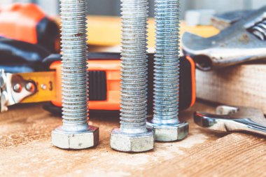 Çelik cıvata somunları ve yıkıtaları ayarlanabilir bir anahtar ve bant ölçüsü yakınında ahşap tahtalar üzerinde yalan.