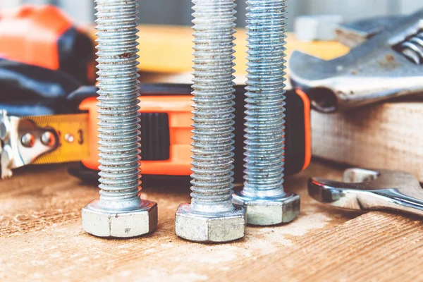 Çelik cıvata somunları ve yıkıtaları ayarlanabilir bir anahtar ve bant ölçüsü yakınında ahşap tahtalar üzerinde yalan.