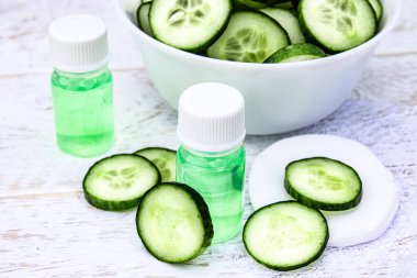 Dilimlenmiş salatalık ve bir şişe salatalık özü Beyaz ahşap masa ve beyaz arka plan üzerinde. Cilt bakımı için sıvı kozmetik.