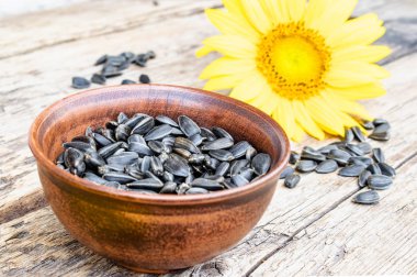 Ahşap bir arka plan üzerinde bir kase sarı ayçiçeği ve ayçiçeği tohumu.