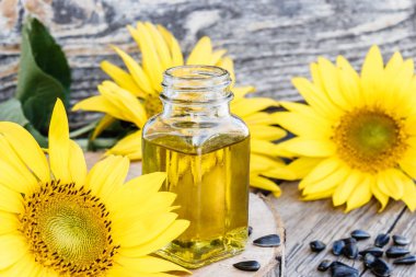 Ahşap bir arka plan üzerinde tohum ve taze çiçekler ile cam bir kavanozda ayçiçek yağı. Sağlıklı gıdalar ve yağlar.