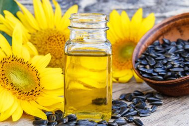 Taze ayçiçeği çiçekleri yakınında ahşap bir arka plan üzerinde bir kase ayçiçek yağı ve ayçiçeği tohumu. Organik ve eko gıda.
