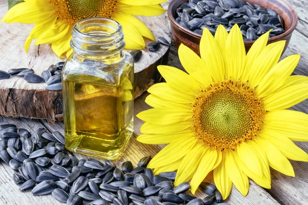 Girasoles y semillas sobre un fondo de madera cerca del aceite de girasol en un frasco de vidrio. Alimentos y grasas saludables . — Foto de Stock